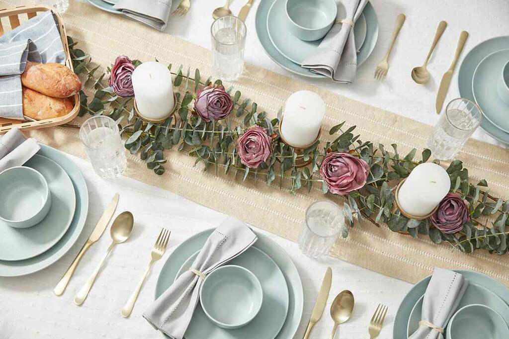 mesa decorada com pratos, talheres, xícaras, flores e velas.
